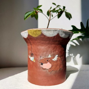 Flying baby hippo painted on dark brown clay planter.